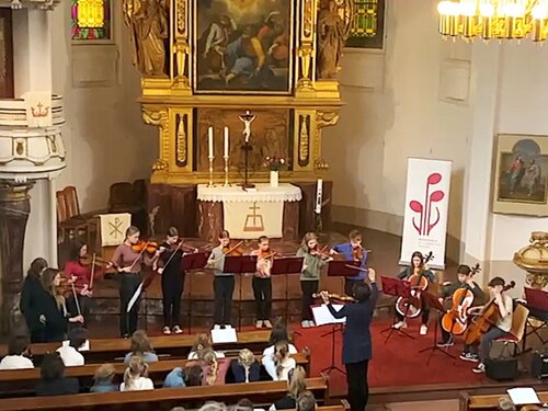 Das Streicherensemble, bestehend aus MusikschülerInnen und einer dirigierenden Lehrerin, spielt vor Publikum in der Kirche Moritzburg. 